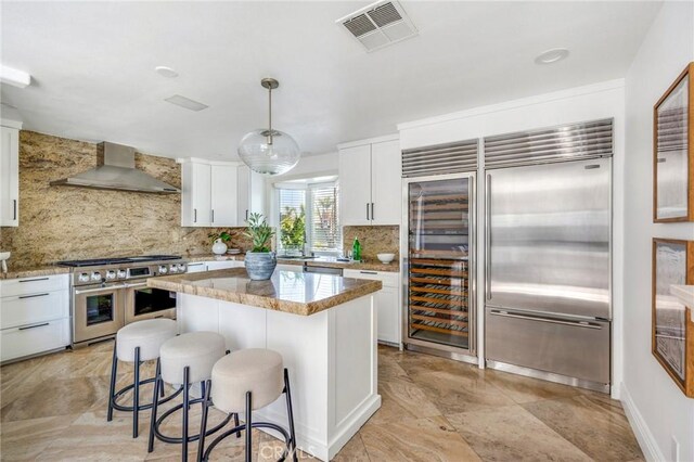 245 Palmer St, Costa Mesa, CA 92627 - kitchen with wall chimney range hood, premium appliances, backsplash, a breakfast bar, and white cabinets