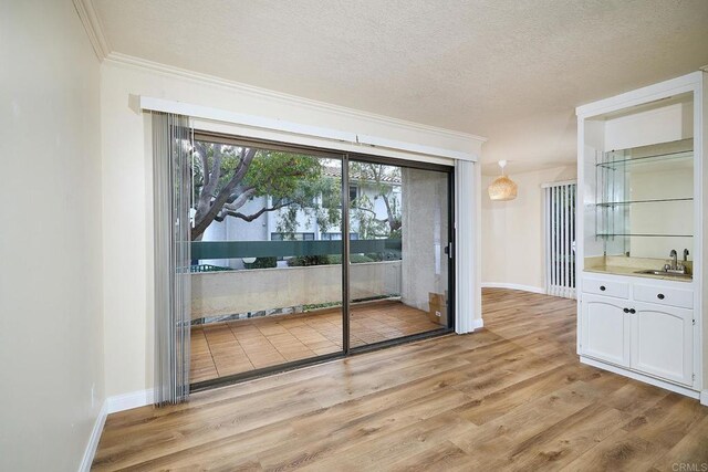 2308 Altisma Way Unit 123, Carlsbad, CA 92009 - unfurnished dining area featuring ornamental molding, light wood-type flooring, a textured ceiling, baseboards, and bar area