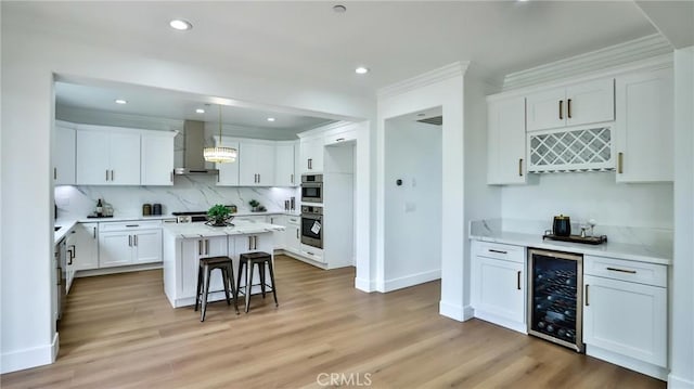 53 Via Armilla, San Clemente, CA 92673 - kitchen featuring beverage cooler, wall chimney range hood, ornamental molding, white cabinetry, and light wood-style flooring