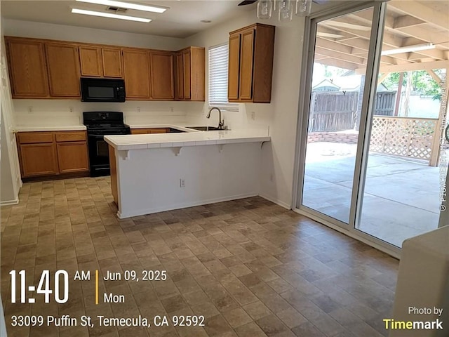 33099 Puffin St, Temecula, CA 92592 - kitchen with black appliances, a peninsula, tile counters, and brown cabinetry
