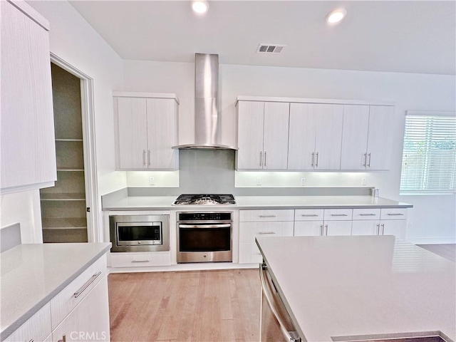 229 Radial, Irvine, CA 92618 - kitchen with appliances with stainless steel finishes, wall chimney exhaust hood, light countertops, light wood-style flooring, and white cabinets