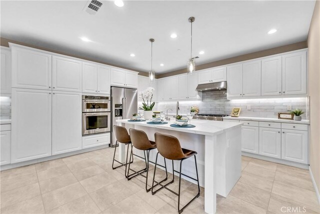 9936 Pear Dr, Westminster, CA 92683 - kitchen featuring under cabinet range hood, appliances with stainless steel finishes, decorative backsplash, a breakfast bar, and white cabinets