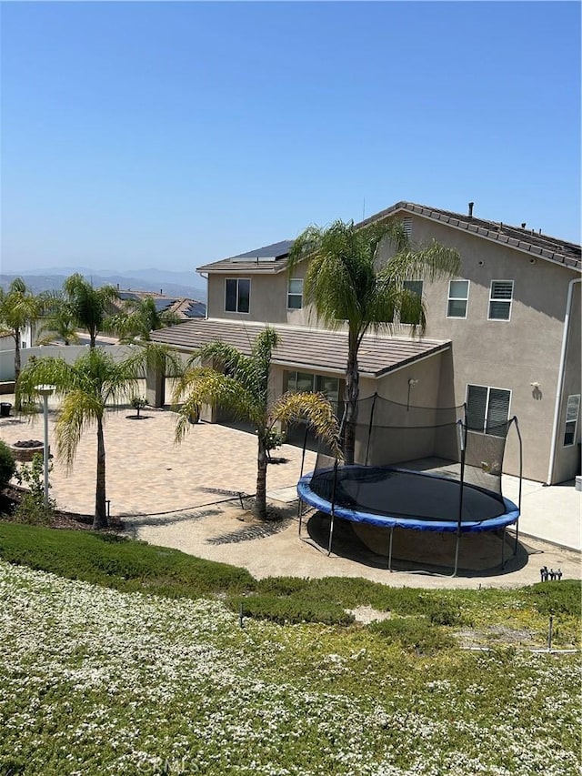 17426 Fairbreeze Ct, Riverside, CA 92504 - back of property featuring a trampoline, stucco siding, solar panels, and a tiled roof
