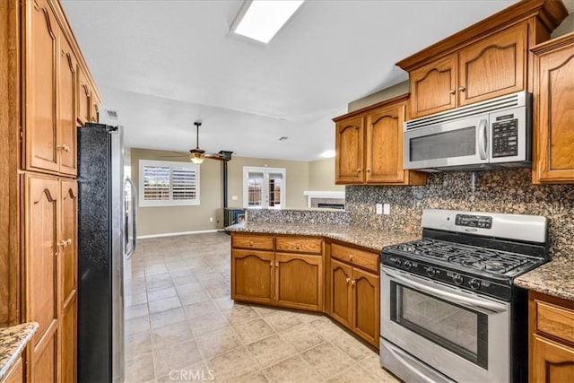 63357 Uranium Rd, Joshua Tree, CA 92252 - kitchen with stainless steel appliances, brown cabinetry, decorative backsplash, a peninsula, and baseboards