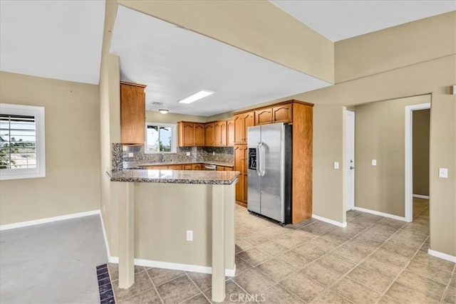 63357 Uranium Rd, Joshua Tree, CA 92252 - kitchen with stainless steel fridge, a peninsula, brown cabinetry, tasteful backsplash, and dark stone countertops