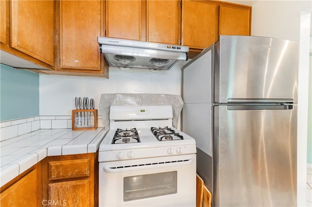 7 Town And Country Rd, Phillips Ranch, CA 91766 - kitchen featuring white gas stove, under cabinet range hood, freestanding refrigerator, tile countertops, and brown cabinets
