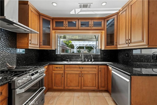 645 Glenmore Blvd, Glendale, CA 91206 - kitchen with wall chimney range hood, stainless steel appliances, a sink, brown cabinets, and dark stone counters