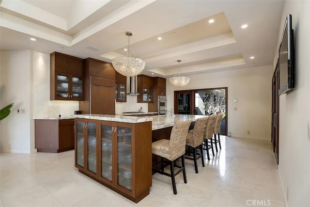 32661 Caribbean Dr, Dana Point, CA 92629 - kitchen featuring a chandelier, a tray ceiling, wall chimney range hood, glass insert cabinets, and recessed lighting