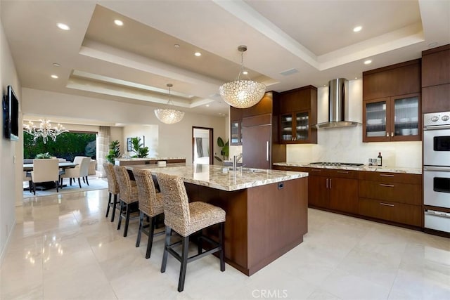 32661 Caribbean Dr, Dana Point, CA 92629 - kitchen with wall chimney range hood, a raised ceiling, stainless steel gas cooktop, a chandelier, and white double oven