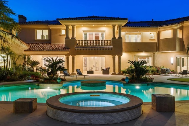 5106 Meadows Del Mar, San Diego, CA 92130 - back of house at night featuring a balcony, a patio, stucco siding, and a pool with connected hot tub