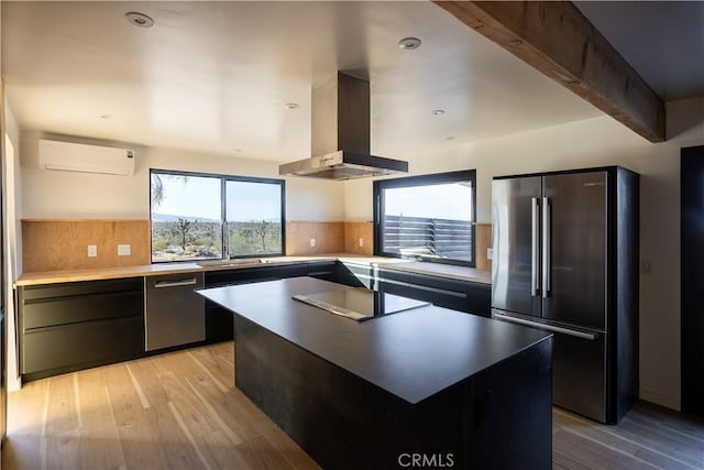 3977 Sage Ave, Yucca Valley, CA 92284 - kitchen featuring appliances with stainless steel finishes, a wall unit AC, wall chimney range hood, light wood-style flooring, and backsplash