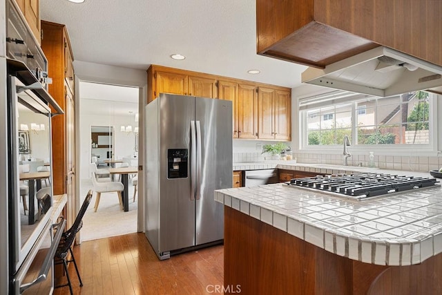 17442 Parker Dr, Tustin, CA 92780 - kitchen with stainless steel appliances, tile counters, a peninsula, light wood finished floors, and backsplash