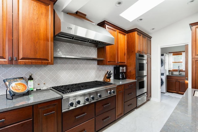 2675 Clove St, San Diego, CA 92106 - kitchen with stacked washer and clothes dryer, appliances with stainless steel finishes, a warming drawer, wall chimney exhaust hood, and vaulted ceiling