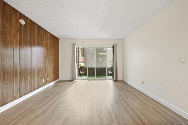 5938 Rancho Mission Rd Unit 133, San Diego, CA 92108 - empty room featuring wood walls, light wood-style floors, baseboards, a textured ceiling, and a smoke detector