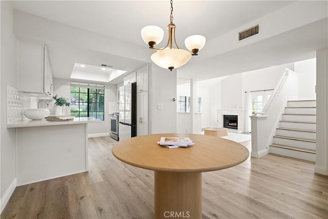 1202 Monte Sereno Dr, Thousand Oaks, CA 91360 - dining space featuring a fireplace with raised hearth, a raised ceiling, light wood-style floors, stairs, and baseboards