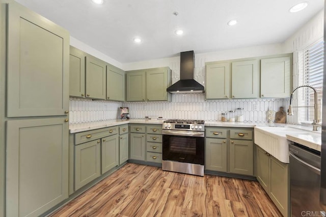 305 Cobblestone Pl, Santee, CA 92071 - kitchen with green cabinetry, wall chimney exhaust hood, appliances with stainless steel finishes, light wood-style flooring, and decorative backsplash