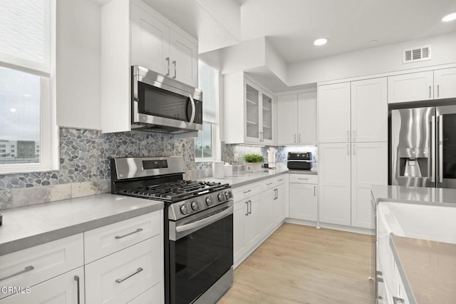 2850 Wagon Wheel Rd Unit 302, Oxnard, CA 93036 - kitchen with appliances with stainless steel finishes, white cabinetry, light countertops, tasteful backsplash, and glass insert cabinets