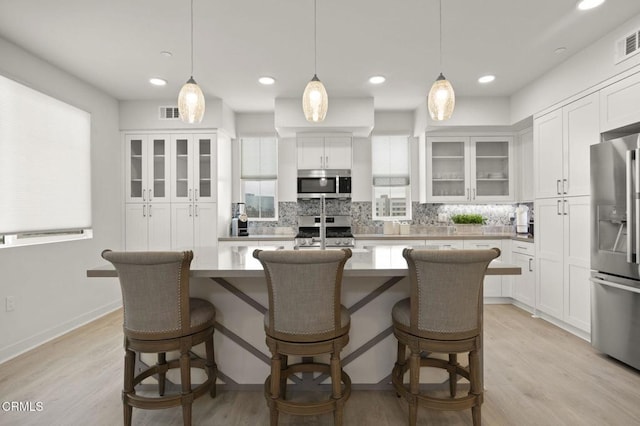2850 Wagon Wheel Rd Unit 302, Oxnard, CA 93036 - kitchen with appliances with stainless steel finishes, backsplash, a center island with sink, white cabinets, and light wood finished floors