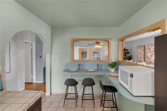 7860 La Fiesta Dr, Buena Park, CA 90620 - kitchen with white microwave, tile counters, arched walkways, a ceiling fan, and light tile patterned floors