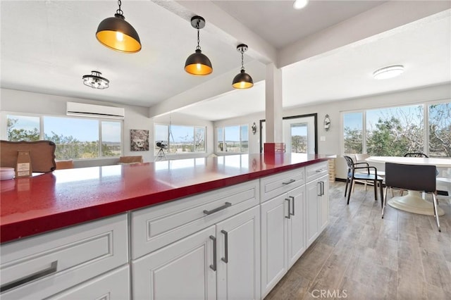 64952 Twentynine Palms Hwy, Joshua Tree, CA 92252 - kitchen featuring light wood finished floors, white cabinetry, a wall unit AC, pendant lighting, and open floor plan