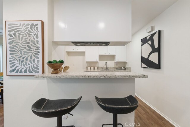 1634 Iowa St Unit B, Costa Mesa, CA 92626 - kitchen featuring white cabinetry, dark wood finished floors, a breakfast bar, baseboards, and light stone countertops