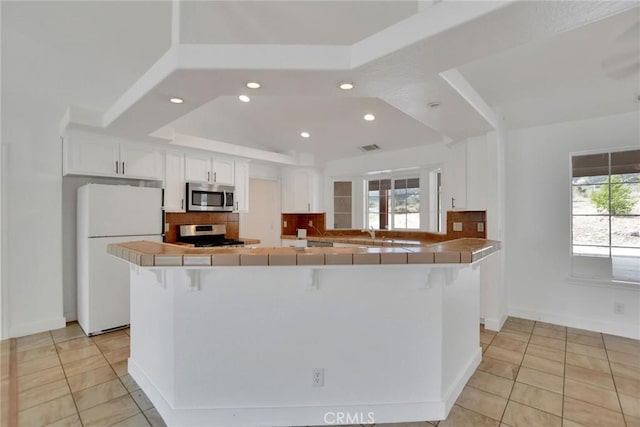 4426 Oil Well Rd, Phelan, CA 92371 - kitchen with stainless steel microwave, freestanding refrigerator, stove, decorative backsplash, and tile counters