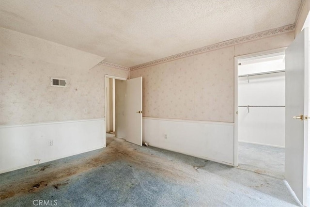 895 Huston Dr, Riverside, CA 92507 - unfurnished bedroom with wallpapered walls, wainscoting, a textured ceiling, carpet, and a walk in closet
