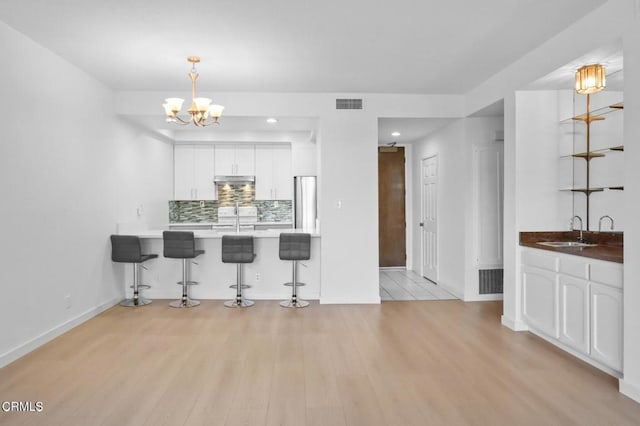 435 La Fayette Park Pl Unit 102, Los Angeles, CA 90057 - kitchen featuring a sink, a kitchen bar, white cabinets, light wood-style floors, and decorative backsplash