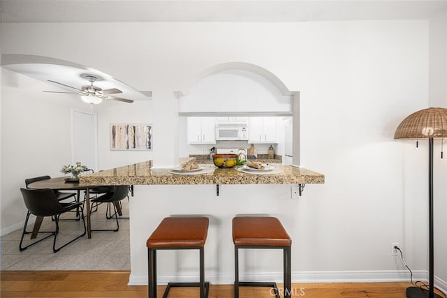 3721 Country Club Dr Unit 18, Long Beach, CA 90807 - kitchen featuring white microwave, a kitchen breakfast bar, white cabinets, and arched walkways