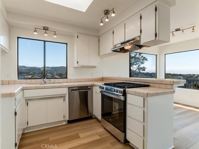 1311 15th St, Los Osos, CA 93402 - kitchen with stainless steel appliances, track lighting, under cabinet range hood, a peninsula, and white cabinetry