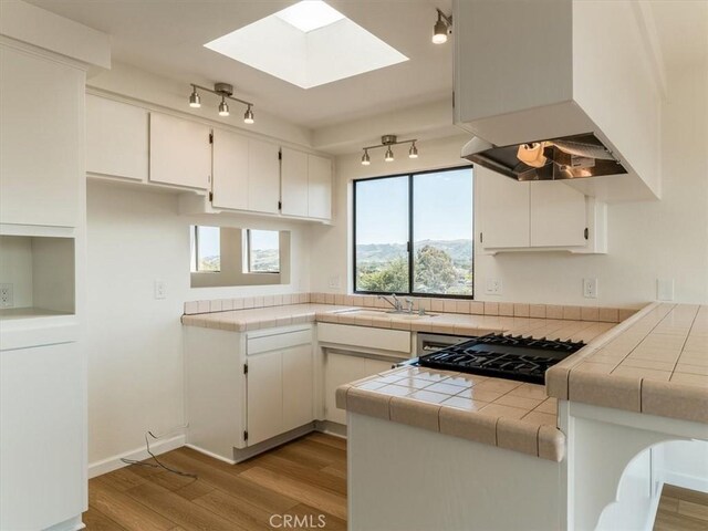 1311 15th St, Los Osos, CA 93402 - kitchen featuring ventilation hood, light wood-type flooring, rail lighting, white cabinets, and a skylight