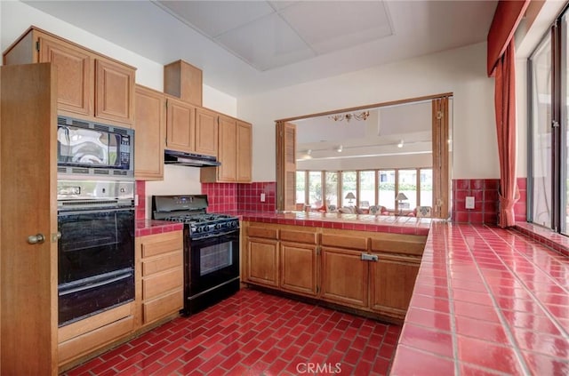 2563 Plaza Del Amo Unit 312, Torrance, CA 90503 - kitchen featuring black appliances, tile counters, a warming drawer, decorative backsplash, and under cabinet range hood