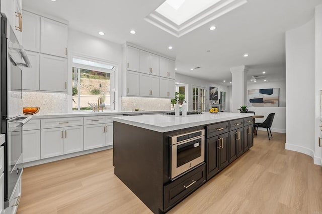 18150 Via Ascenso, Rancho Santa Fe, CA 92067 - kitchen featuring white cabinetry, light wood-style flooring, tasteful backsplash, light countertops, and a center island