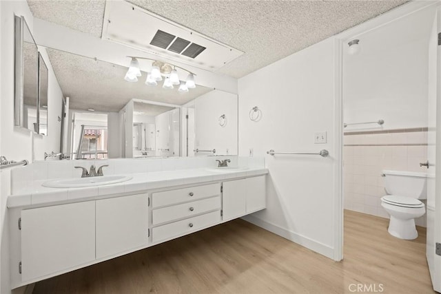 1127 E Del Mar Blvd Unit 235, Pasadena, CA 91106 - full bath featuring wood finished floors, a textured ceiling, toilet, double vanity, and tile walls