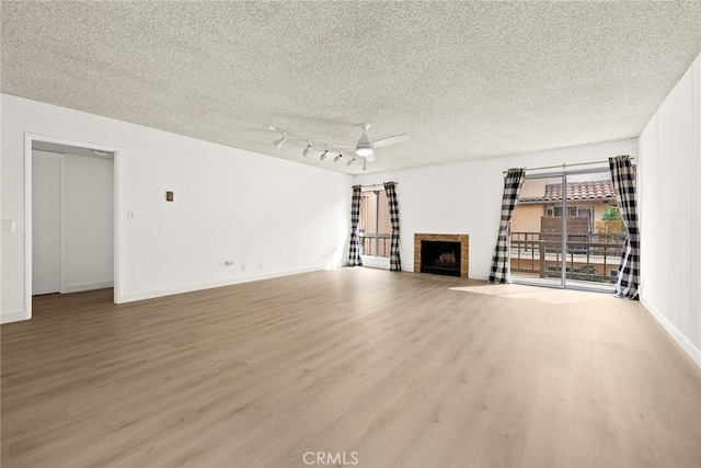 1127 E Del Mar Blvd Unit 235, Pasadena, CA 91106 - unfurnished living room with light wood-type flooring, a textured ceiling, a ceiling fan, a fireplace, and baseboards