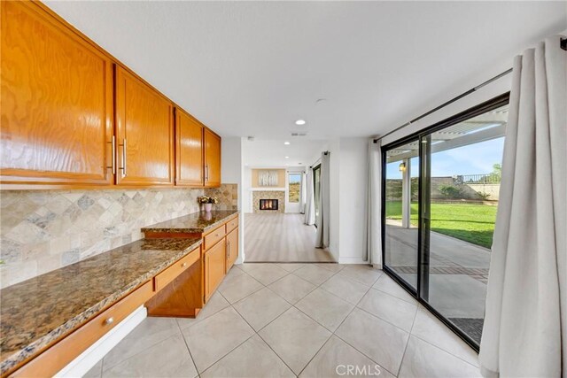 867 Winding Brook Ln, Walnut, CA 91789 - kitchen with backsplash, dark stone countertops, light tile patterned floors, brown cabinets, and a warm lit fireplace