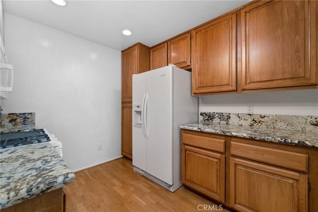 2916 Luciernaga St Unit A, Carlsbad, CA 92009 - kitchen featuring white fridge with ice dispenser, brown cabinetry, light wood finished floors, light stone counters, and stove