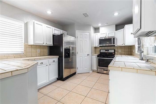 6683 Sherman Hoyt Ave Unit 29, Palms, CA 92277 - kitchen featuring appliances with stainless steel finishes, tile counters, tasteful backsplash, white cabinets, and light tile patterned flooring