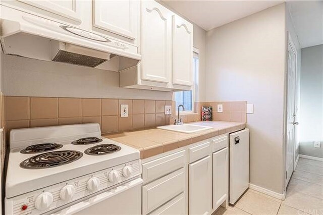 6683 Sherman Hoyt Ave Unit 29, Palms, CA 92277 - kitchen with electric range, under cabinet range hood, a sink, white cabinets, and tile counters