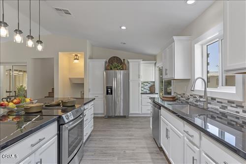 22150 Buena Vista St, Tehachapi, CA 93561 - kitchen with stainless steel appliances, vaulted ceiling, a sink, tasteful backsplash, and white cabinets