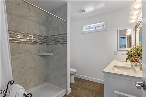 22150 Buena Vista St, Tehachapi, CA 93561 - bathroom featuring double vanity, tiled shower, and wood finished floors
