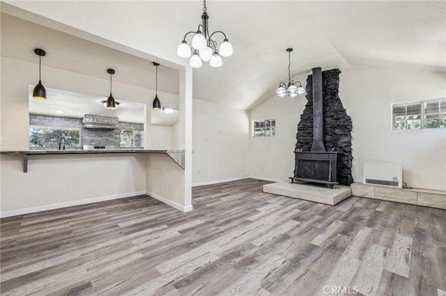 1850 Pond, Big Bear City, CA 92314 - unfurnished living room featuring a chandelier, wood finished floors, vaulted ceiling, a wood stove, and healthy amount of natural light