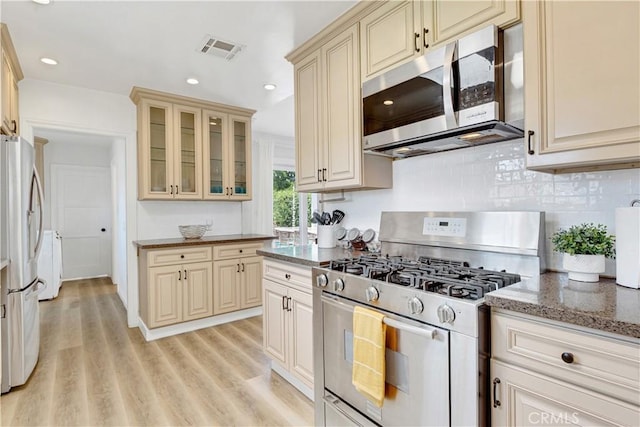 4901 Ethel Ave, Sherman Oaks, CA 91423 - kitchen featuring appliances with stainless steel finishes, cream cabinets, light wood-style floors, glass insert cabinets, and dark stone countertops