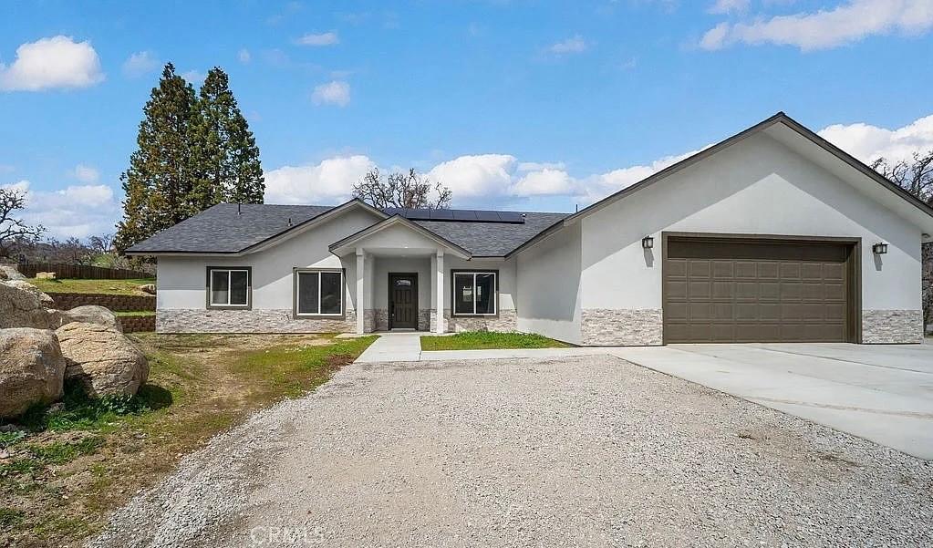 30181 Knight Ct, Tehachapi, CA 93561 - view of front facade featuring stone siding, stucco siding, roof mounted solar panels, and an attached garage