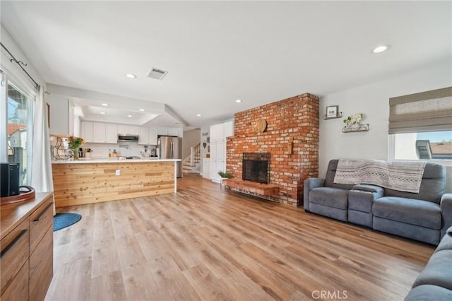 7906 Appaloosa Ct, Rancho Cucamonga, CA 91701 - living room with healthy amount of natural light, light wood-style floors, recessed lighting, a brick fireplace, and stairs