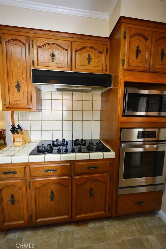 11514 Beverly Blvd, Whittier, CA 90601 - kitchen with appliances with stainless steel finishes, tile countertops, under cabinet range hood, ornamental molding, and brown cabinets