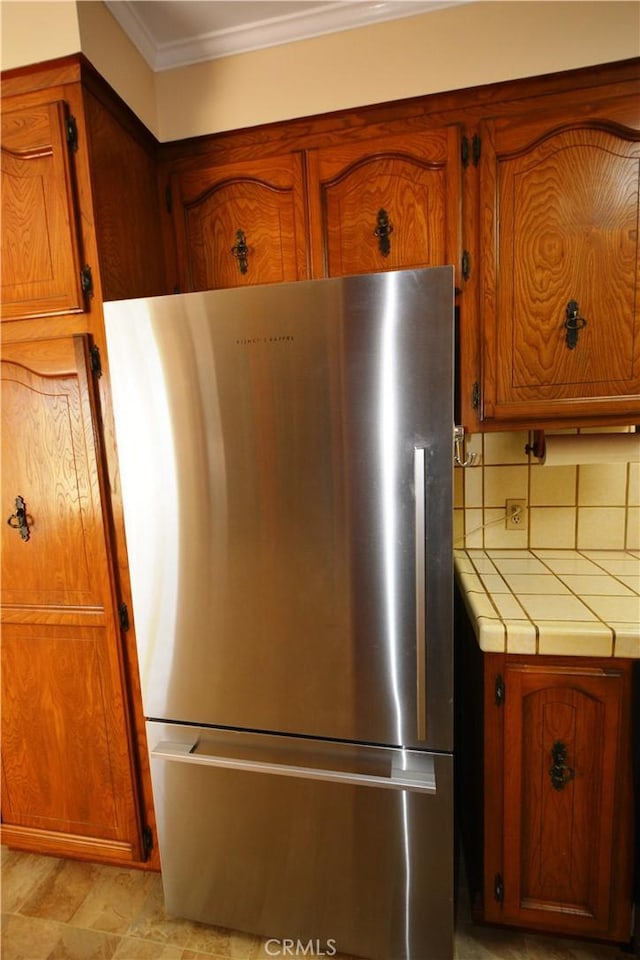 11514 Beverly Blvd, Whittier, CA 90601 - detailed view of freestanding refrigerator, crown molding, tile countertops, and brown cabinetry