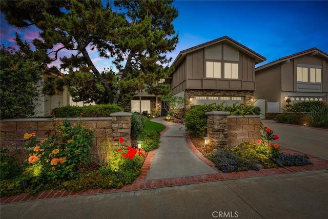 3595 Sego St, Irvine, CA 92606 - tudor house featuring a garage, driveway, stone siding, board and batten siding, and stucco siding