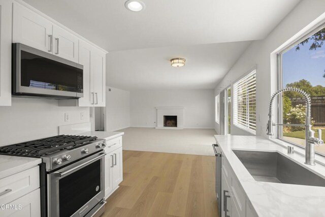 196 Mariposa Dr, Camarillo, CA 93012 - kitchen with stainless steel appliances, a sink, light wood-style floors, a fireplace, and white cabinetry
