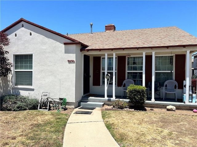 1923 W 115th St, Los Angeles, CA 90047 - doorway to property featuring covered porch, a lawn, a chimney, stucco siding, and a shingled roof